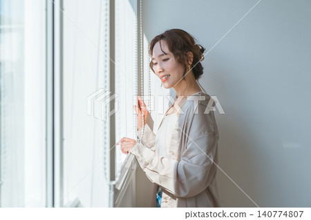 一位衣著時尚的女士站在客廳窗邊。 一位衣著時尚的女士站在客廳窗邊。 140774807
