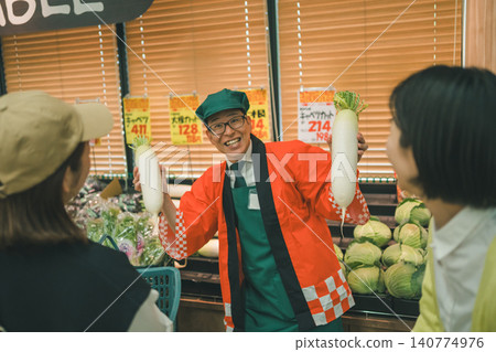 A shop employee in a happi coat calls out to customers, holding up a radish. A shop employee in a happi coat calls out to customers, holding up a radish. 140774976
