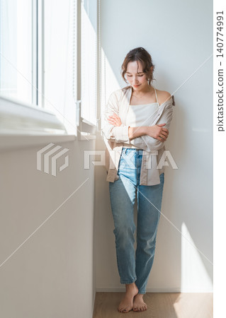 A woman (model, fashion) standing by a window bathed in sunlight. A woman (model, fashion) standing by a window bathed in sunlight. 140774991