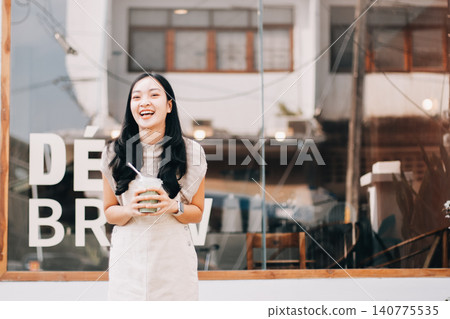 Young woman drinking iced coffee outside a chocolate shop Young woman drinking iced coffee outside a chocolate shop 140775535