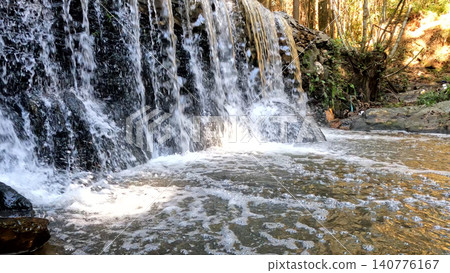 Small artificial waterfall cascading into a rocky stream 140776167