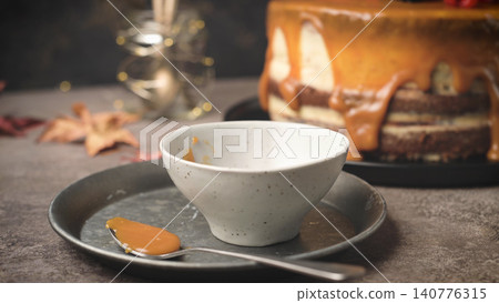 Caramel drip cake with a small bowl and spoon of sauce Caramel drip cake with a small bowl and spoon of sauce 140776315