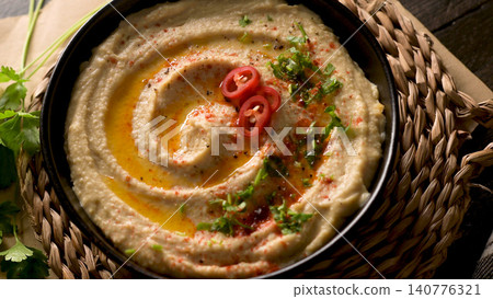 Creamy hummus bowl garnished with chili and fresh herbs 140776321