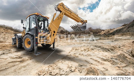A universal excavator loader is busy moving dirt at a construction site. The machine is equipped with a loader and an excavator arm A universal excavator loader is busy moving dirt at a construction site. The machine is equipped with a loader and an excavator arm 140776704
