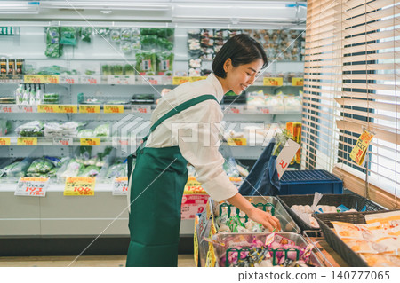 A smiling female supermarket employee arranging garlic on the shelves. A smiling female supermarket employee arranging garlic on the shelves. 140777065