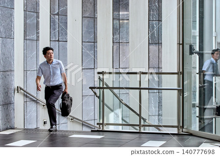 A Japanese businessman in his 30s, wearing a short-sleeved shirt, climbs the stairs of an office building on his way to work. A Japanese businessman in his 30s, wearing a short-sleeved shirt, climbs the stairs of an office building on his way to work. 140777698