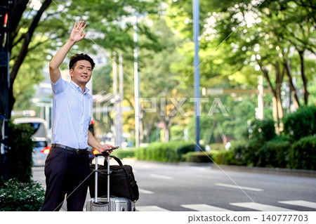 一位商務人士提著行李箱，在出差途中，用智慧型手機上的叫車軟體預訂了一輛計程車，正在等待司機。 140777703