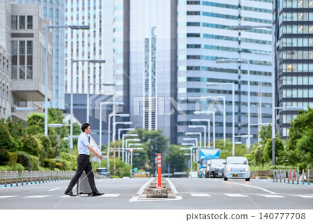 一名三十多歲的日本男子,因公出差,拖著手提行李箱走過城市辦公區的行人過馬路。 一名三十多歲的日本男子,因公出差,拖著手提行李箱走過城市辦公區的行人過馬路。 140777708