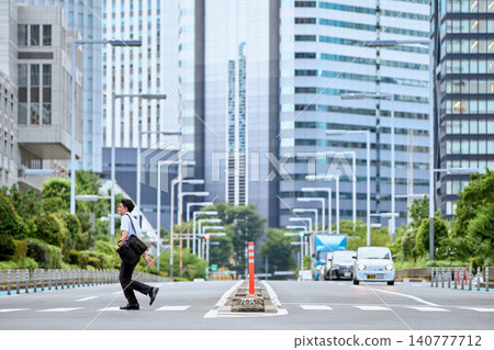 A Japanese man in his 30s, wearing a short-sleeved shirt, runs across a pedestrian crossing on a city street lined with skyscrapers. A Japanese man in his 30s, wearing a short-sleeved shirt, runs across a pedestrian crossing on a city street lined with skyscrapers. 140777712