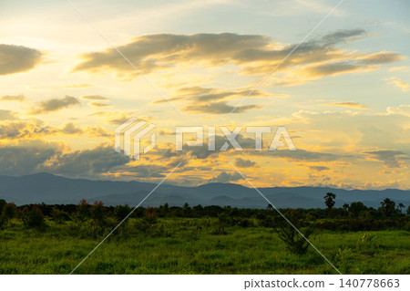 Scenic landscape of green grass field and mountains under golden sunset sky. 140778663