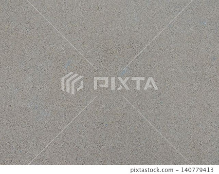 A fine-grained matte texture in a gray-beige color. The uniform, rough surface resembles polished concrete, granite chips, or plaster with occasional inclusions. The background is neutral and minimal 140779413