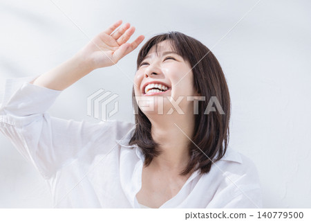 一位女子麵帶微笑，用手遮擋著刺眼的光線。 140779500