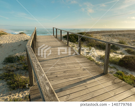 Wooden walkway leading to the scenic ocean shore at Furadouro beach in Ovar Portugal, captured on a bright and calm summer afternoon Wooden walkway leading to the scenic ocean shore at Furadouro beach in Ovar Portugal, captured on a bright and calm summer afternoon 140779768