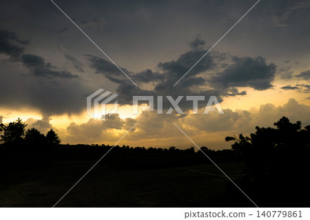 This dramatic scene depicts a stormy sunset with clouds breaking to reveal golden light. The atmosphere resembles a rare optical weather phenomenon, where sunset colours glow behind dark storm clouds This dramatic scene depicts a stormy sunset with clouds breaking to reveal golden light. The atmosphere resembles a rare optical weather phenomenon, where sunset colours glow behind dark storm clouds 140779861