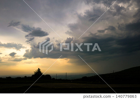 This dramatic scene depicts a stormy sunset with clouds breaking to reveal golden light. The atmosphere resembles a rare optical weather phenomenon, where sunset colours glow behind dark storm clouds This dramatic scene depicts a stormy sunset with clouds breaking to reveal golden light. The atmosphere resembles a rare optical weather phenomenon, where sunset colours glow behind dark storm clouds 140779863