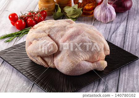 Raw whole chicken on black plate with cherry tomatoes garlic and herbs on rustic wood Raw whole chicken on black plate with cherry tomatoes garlic and herbs on rustic wood 140780102