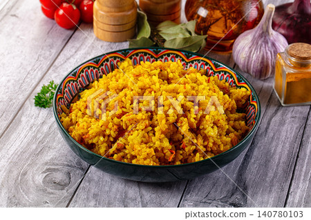 Yellow spiced rice in patterned bowl with garlic and tomatoes on rustic wood 140780103
