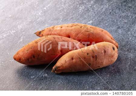 Three raw sweet potatoes on textured gray surface Three raw sweet potatoes on textured gray surface 140780105