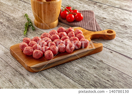 Raw meatballs on wooden cutting board with cherry tomatoes and rosemary Raw meatballs on wooden cutting board with cherry tomatoes and rosemary 140780130