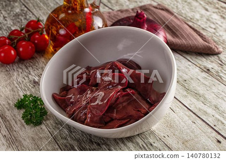 Raw liver in white bowl with cherry tomatoes parsley red onion and oil bottle on rustic wood Raw liver in white bowl with cherry tomatoes parsley red onion and oil bottle on rustic wood 140780132