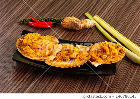 Grilled scallops with yellow sauce on black plate surrounded by lemongrass chili and galangal Grilled scallops with yellow sauce on black plate surrounded by lemongrass chili and galangal 140780145
