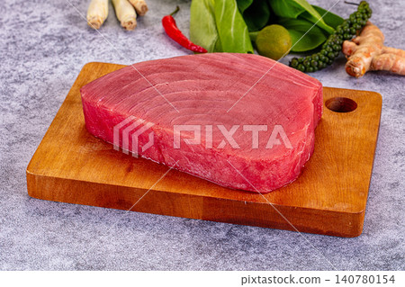 Raw tuna steak on wooden cutting board with fresh herbs and spices Raw tuna steak on wooden cutting board with fresh herbs and spices 140780154