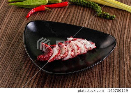 Sliced octopus on black plate with chili peppers and herbs Sliced octopus on black plate with chili peppers and herbs 140780159