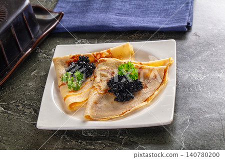 Folded crepes topped with black caviar and fresh parsley on white plate Folded crepes topped with black caviar and fresh parsley on white plate 140780200