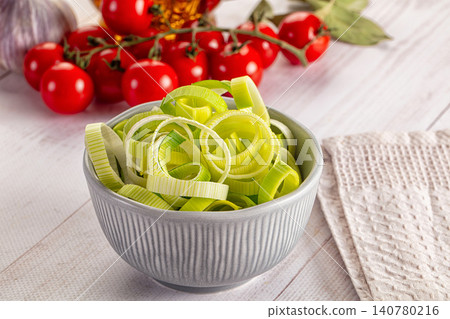 Sliced leeks in ceramic bowl with cherry tomatoes and garlic on white wood 140780216