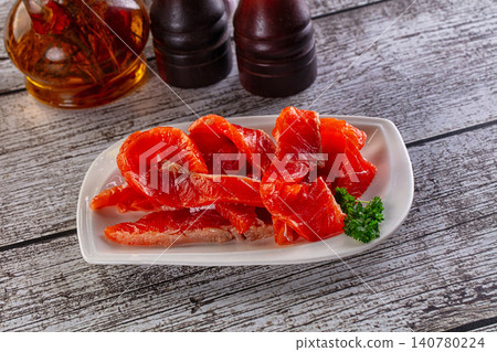 Sliced smoked salmon on white plate with parsley garnish and condiments on rustic wooden table Sliced smoked salmon on white plate with parsley garnish and condiments on rustic wooden table 140780224