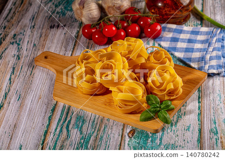 Fresh pasta nests with basil cherry tomatoes and garlic on rustic wooden board Fresh pasta nests with basil cherry tomatoes and garlic on rustic wooden board 140780242