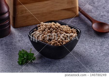 White peppercorns in black bowl with parsley and wooden spoon on gray surface White peppercorns in black bowl with parsley and wooden spoon on gray surface 140780249