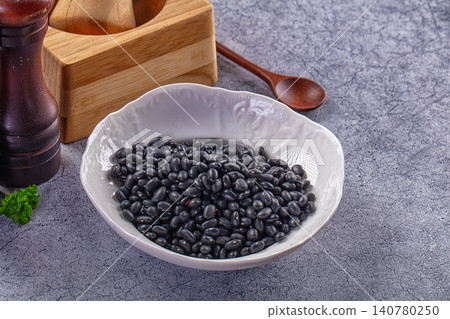 Black beans in white ceramic bowl with wooden spoon and pepper mill on gray textured surface Black beans in white ceramic bowl with wooden spoon and pepper mill on gray textured surface 140780250