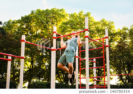 Fit man doing a pullup exercise during an outdoor street workout. Physical strength training and calisthenics fitness sport concept in the park. Fit man doing a pullup exercise during an outdoor street workout. Physical strength training and calisthenics fitness sport concept in the park. 140780354