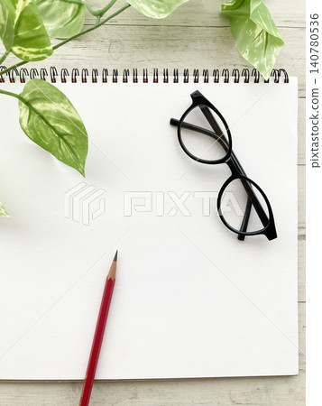 Ideas and lifestyle, a blank sketchbook, black-rimmed glasses and a pencil, houseplants and a plain white ring notebook. 140780536