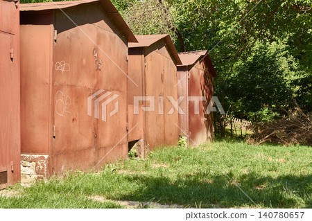 Old brown metal garages. Row of iron sheds in a yard. Rusty garage boxes outdoors. Old brown metal garages. Row of iron sheds in a yard. Rusty garage boxes outdoors. 140780657
