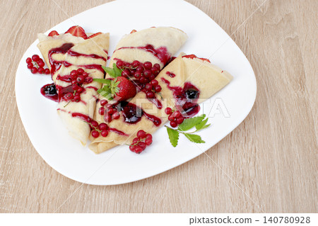 Pancakes with cranberries and strawberries on a plate. Pancakes with berries, strawberries and chocolate syrup. Breakfast with pancakes with strawberries and berries on a plate. Pancakes with cranberries and strawberries on a plate. Pancakes with berries, strawberries and chocolate syrup. Breakfast with pancakes with strawberries and berries on a plate. 140780928