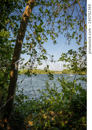 Mercers Lake near Merstham, Surrey, UK. View through trees to the lake. Boats are moored on the water. Mercers Lake near Merstham, Surrey, UK. View through trees to the lake. Boats are moored on the water. 140782369