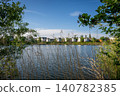 A modern housing development next to the Holmethorpe Lagoons in Mersham, Surrey, UK. Trees and reeds in the foreground. Landscape orientation. Focus on foreground. 140782385