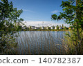 A modern housing development next to the Holmethorpe Lagoons in Mersham, Surrey, UK. Trees and reeds in the foreground. Landscape orientation. 140782387
