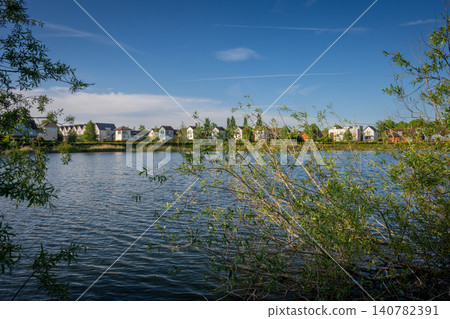 A modern housing development next to the Holmethorpe Lagoons in Mersham, Surrey, UK. Trees in the foreground. Landscape orientation. A modern housing development next to the Holmethorpe Lagoons in Mersham, Surrey, UK. Trees in the foreground. Landscape orientation. 140782391