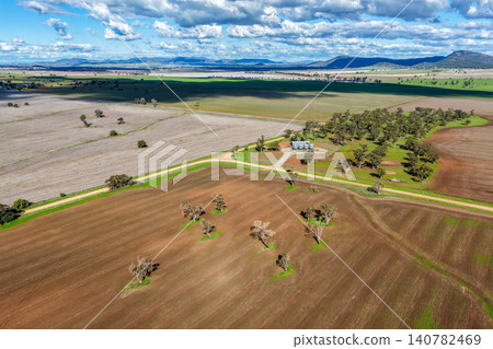 Aerial view of cultivated agricultural fields surrounded by lush green landscape, with a dirt road leading through the farmland, highlighting rural patterns and textures in NSW, Australia. Aerial view of cultivated agricultural fields surrounded by lush green landscape, with a dirt road leading through the farmland, highlighting rural patterns and textures in NSW, Australia. 140782469
