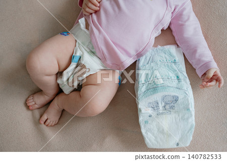 Detailed close-up shot focused on babys chubby legs, wearing a modern disposable diaper, with another fresh diaper lying next to the infant. Gentle macro view of newborn soft skin and diaper changing Detailed close-up shot focused on babys chubby legs, wearing a modern disposable diaper, with another fresh diaper lying next to the infant. Gentle macro view of newborn soft skin and diaper changing 140782533