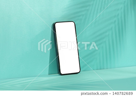 Smartphone mockup with blank screen on mint green background with palm leaf shadow Smartphone mockup with blank screen on mint green background with palm leaf shadow 140782689