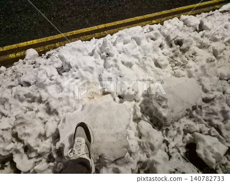 Foot stepping into dirty snow beside roadside curb Foot stepping into dirty snow beside roadside curb 140782733