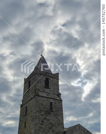 Stone church tower beneath dramatic cloudy sky Stone church tower beneath dramatic cloudy sky 140782760