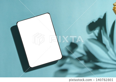 Tablet mockup with blank white screen on light blue background with plant shadows 140782801