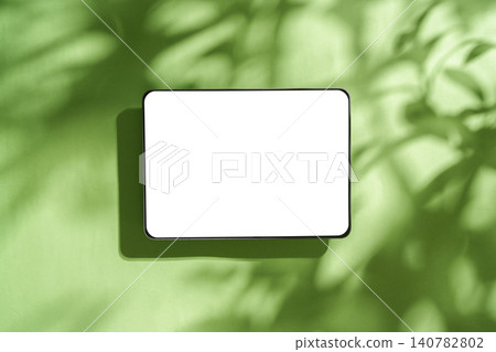 Digital tablet mockup with blank white screen on green background with leaf shadows Digital tablet mockup with blank white screen on green background with leaf shadows 140782802