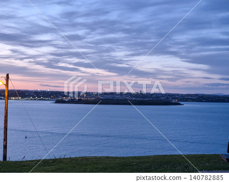 Twilight coastal landscape with calm water and city lights Twilight coastal landscape with calm water and city lights 140782885