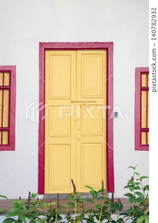 Yellow wooden door on white colonial facade with pink window frames Yellow wooden door on white colonial facade with pink window frames 140782932